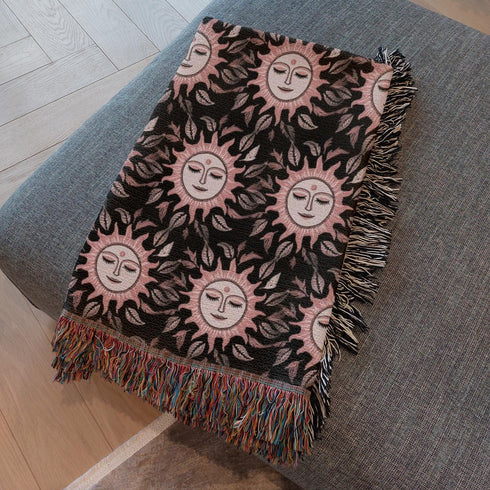 Luxurious woven cotton throw featuring dreamy blush pink sun faces with closed eyes against black background with delicate ray patterns and elegant fringe trim. Perfect celestial wall hanging, witchy bedroom decor, or dark academia throw blanket.